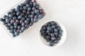 Open clamshell container of blueberries on a white granite counter, small white bowl