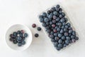 Open clamshell container of blueberries on a white granite counter, small white bowl