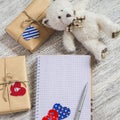 Open clean Notepad, homemade Valentine's day gifts in kraft paper, paper hearts, toy bear on white wooden table.