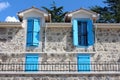 Open and closed light blue wooden window blinds on windows of newly built Mediterranean villa in traditional stone style with