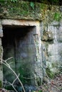 Open dark spooky entrance to the catacomb with peeling concrete and green moss