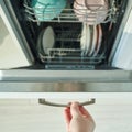 Open dishwasher with clean dishes and hand holding handle in modern kitchen Royalty Free Stock Photo