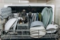 Open dishwasher close up clogged with clean washed dishes. dry cutlery closeup. spoons forks. mugs, plates. household appliances Royalty Free Stock Photo