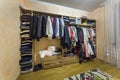 Open dressing closet wardrobe full of different male and female colorful clothes and accessories on hangers and shelf. Modern