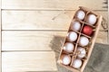 Open eco-friendly wooden box with white eggs and one red Easter egg on wooden background. Royalty Free Stock Photo