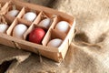Open eco-friendly wooden box with white eggs and one red Easter egg on rough burlap. Royalty Free Stock Photo