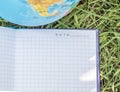 An open empty notebook lies on the grass near the globe, the concept of ecology and back to school, school summer holidays, a