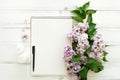 Open empty notebook surrounded with lilac flowers on white wooden background. Flat lay, top view, copy space Royalty Free Stock Photo