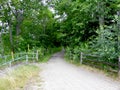 Open entrance with wooden fence to the forest. Gravel pathway to the green woods