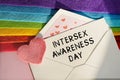 An open envelope with the text TRANSGENDER AWARENESS WEEK, on a pink and blue background with a decor of felt hearts and a flower