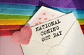 An open envelope with the textI NATIONAL Coning Out DAY, on a pink and blue background with a decor of felt hearts and a flower. Royalty Free Stock Photo