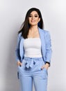 Open and friendly business woman in blue official suit stands with her hands in her pockets on white