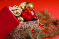 Open gift box with red and golden Christmas baubles and pearl beads on the red background. Near the spruce branch Royalty Free Stock Photo