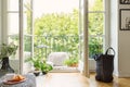 Open glass door from a living room interior into a city garden on a sunny balcony with green plants