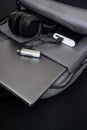 An open gray urban backpack containing a USB card reader power bank wireless headphones and a silver laptop or ultrabook