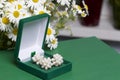 An open green velvet box for jewelry. In it lies a set: a ring and earrings with pearls. Next to the vase is a bouquet of chamomil Royalty Free Stock Photo