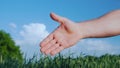 An open hand stretched out for the handshake of a man`s hand. Against the background of a green wheat field and a blue Royalty Free Stock Photo