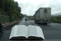 Open Hebrew Holy Bible on stormy day and heavy rain. Blurred background with expressway and cars.