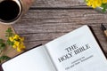 Open holy bible book with a cup of coffee, pen, vintage paper, and spring flowers on wooden table, top view Royalty Free Stock Photo