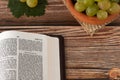 Open Holy Bible Book with fresh ripe grapes in a bowl on wooden table