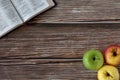 Open Holy Bible Book and three apples in various colors on wooden background with copy space, top view Royalty Free Stock Photo