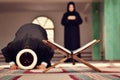 An open Holy quran with wood stand with praying people in background