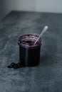 Open a jar of berry jam with a spoon in the middl. jam flowing along the wall of the jars on the table