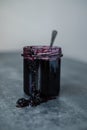 Open a jar of berry jam with a spoon in the middl. jam flowing along the wall of the jars on the table