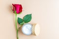 Open jar with face or body cream with red rose on beige background. Skin care anti aging cosmetics product presentation Royalty Free Stock Photo