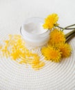 Open jar filled with cream and dandelion on white