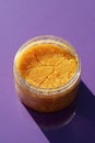 Open jar with orange sugar body scrub texture on a purple background. Royalty Free Stock Photo