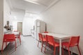 Open kitchen with two red dining tables and chairs, several refrigerators