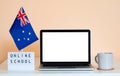 Open laptop with a blank white screen sits on a table next to the Australian flag and a display that says Online School.