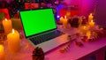 An open laptop with a chroma key on the screen lies on a white wooden table. Christmas gifts, burning candles, cones, confetti,