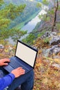 An open laptop is kneeling by a tourist sitting on a rock.