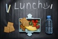 Open lunch box with banana berries and crackers and a bottle of water on a black background with colorful crayons and lunch