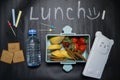 Open lunch box with banana berries and crackers and a bottle of water on a black background with colorful crayons and lunch
