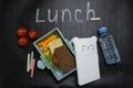 Open lunch box with a sandwich of whole grain bread, cheese, green salad, tomato, cucumber and a bottle of water on a