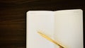 An open note book with a golden pen on a wooden background.