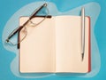 Open note, pen and eyeglasses top view on blue table Royalty Free Stock Photo