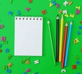 Open notebook with blank white sheets in line, colored wooden pencils on a green background with scattered wooden letters Royalty Free Stock Photo