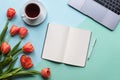 Open notebook on blue background with tulips, cup of tea and laptop. Copy space. Royalty Free Stock Photo