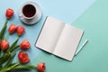 Open notebook on blue background with tulips, cup of tea and laptop. Copy space. Royalty Free Stock Photo