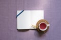 Open notebook and color pencil, cup of black tea on purple check pattern fabric background. top view, copy space Royalty Free Stock Photo