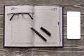 Open notebook diary with a pen for notes, mobile phone screen mock up on a wooden table Royalty Free Stock Photo