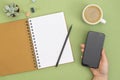 Open notebook with empty page, pencil, coffee cup and hand holding a smartphone. Table top, work space on green background. Royalty Free Stock Photo