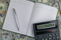 An open notebook with a pen and calculator stand on a pile of dolar banknotes Royalty Free Stock Photo