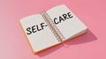 Open notebook with 'SELF-CARE' written prominently, set against a soft pink background. Royalty Free Stock Photo
