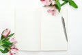 An open notebook with a steel pen on a white wooden background with flowers. Minimal composition, home women`s office Royalty Free Stock Photo