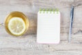 An open notebook on a wooden table, next to stand a silver pen and a cup of mint tea with lemon Royalty Free Stock Photo